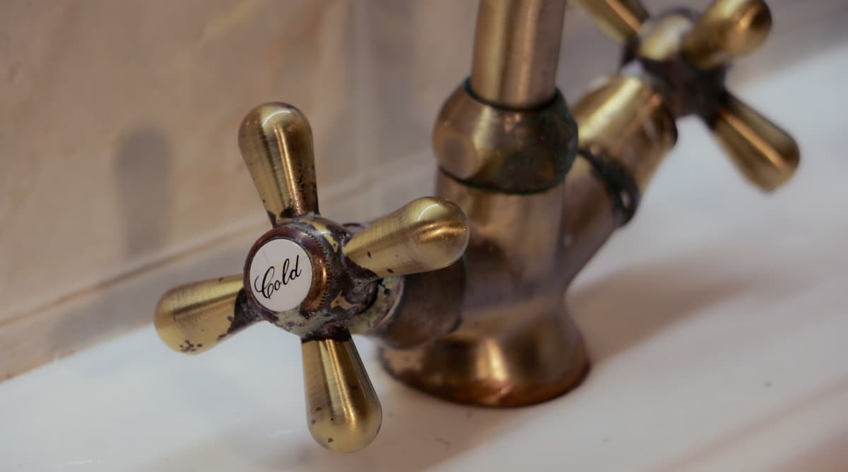 Close-up of an antique brass cross-handle faucet showing wear around the cold water valve